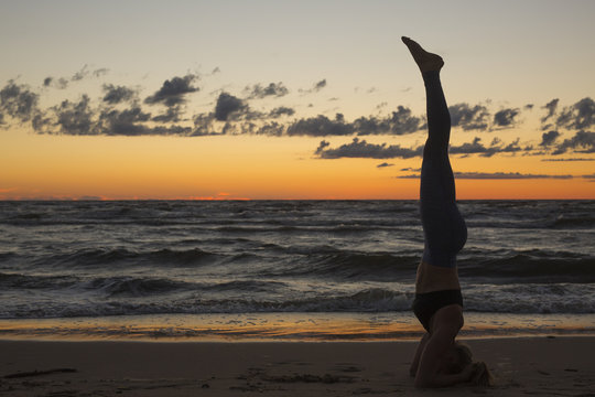 Harmonious landscape with a woman practicing yoga upside-down by the sea at sunset.