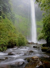 Large waterfall cascading down into a shallow pool and flowing stream. © mat_millard