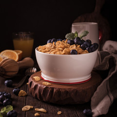 Healthy breakfast with corn flakes, berries and milk on old dark wooden background. Copy space. Retro style toned.