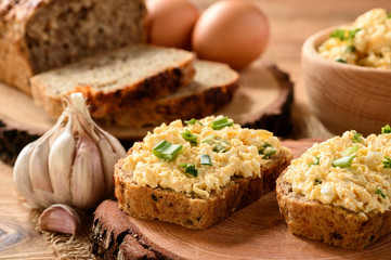 Whole wheat sandwiches with egg and cheese spread on wooden stump.