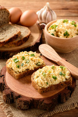 Whole wheat sandwiches with egg and cheese spread on wooden stump.