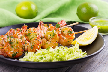 Cilantro grilled shrimps on skewers with sesame napa cabbage, green butter sauce and lemon. Skewered prawns on black plate