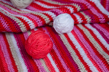 small yarn balls on crocheted striped fabric in red colors