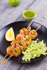 Cilantro grilled shrimps on skewers with sesame napa cabbage, green butter sauce and lemon. Skewered prawns on black plate