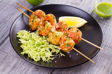 Cilantro grilled shrimps on skewers with sesame napa cabbage, green butter sauce and lemon. Skewered prawns on black plate