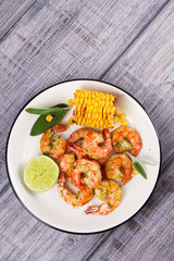 Grilled shrimps and corn garnished with lime and sage leaves. Prawns on white plate. View from above, top studio shot
