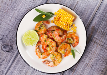 Grilled shrimps and corn garnished with lime and sage leaves. Prawns on white plate. View from above, top studio shot