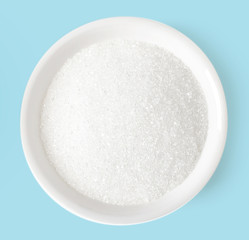 Bowl of sugar on blue background, top view