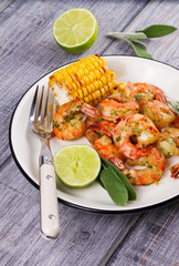 Grilled shrimps and corn garnished with lime and sage leaves. Prawns on white plate