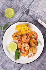 Grilled shrimps and corn garnished with lime and sage leaves. Prawns on white plate. View from above, top studio shot