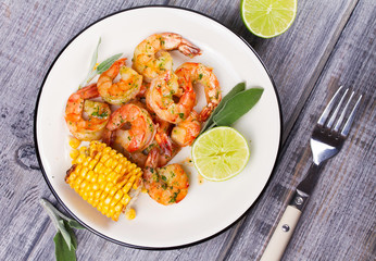 Grilled shrimps and corn garnished with lime and sage leaves. Prawns on white plate. View from above, top studio shot