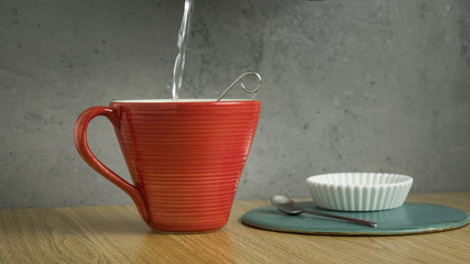 Pouring hot water in red tea cup. Breakfast or afternoon drink.