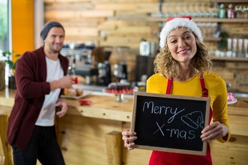 Smiling waitress standing with merry x mas sign board in cafe