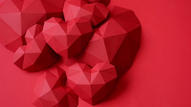 Heap of red polygonal paper heart shapes on red background, top view, rotating video