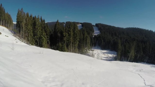 Ski lift ride clip, side view, with snow covered ski trails below, mountains and trees in the background and vacant ski chairs passing by