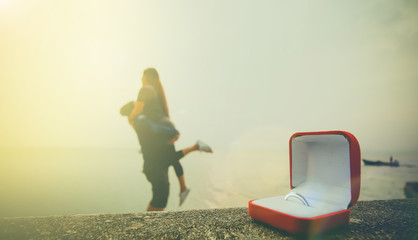 Close up wedding ring in red box with abstract blurred of human holding together on sunset time at the beach and sunlight