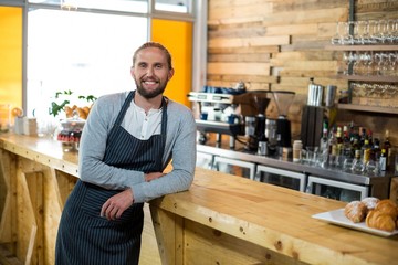 Portrait of smiling waiter leaning at counter
