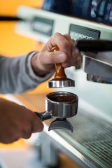 Waiter using a tamper to press ground coffee into a portafilter