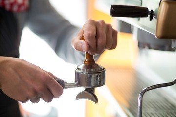 Waiter using a tamper to press ground coffee into a portafilter