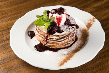 Chocolate Pancakes with Vanilla Ice Cream and Warm Cherry Sauce on white plate