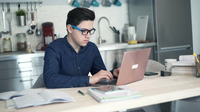 Young tired, overworked teenager doing homework on laptop computer at home
