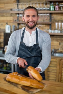 Portrait of waiter cutting bread at counter