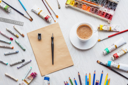 Designer desk with colored crayons, brush, pencils and paints, cup of coffee. Top view . Flat lay image.Working desk table concept.