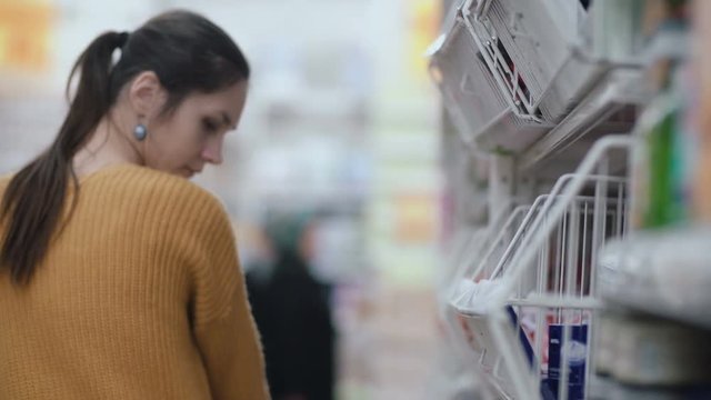 Young beautiful woman in supermarket standing in front shelfs and looking to something, then turns and walking away. 4K