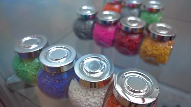 Samples of multi-colored plastic pellets in transparent containers. In the jars are blue, white, green, red, yellow, pink, grey polymer granules. Shot in motion