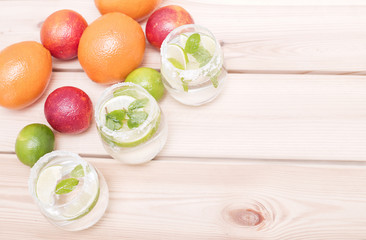 Three glasses of water with lime and mint, fruit background, top view