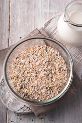 Raw oat flakes in  the  glass bowl on the  white wooden table top view