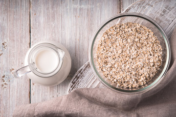 Raw oat flakes  and milk jug on the  white wooden table top view