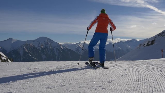 Woman puts boots to skis and goes down the slope on a background of snowy mountains