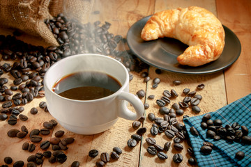 Hot coffee cup and breakfast baked croissants with alarm clock on wooden background