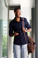 happy young black man walking with tablet and bag