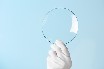 Scientist hand in glove show circle piece of new research prototype of transparent clear glass or...