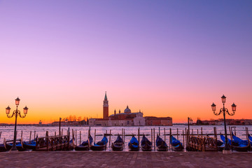 Traditional Italian gondolas moored to the poles in Europe Venice near the city center and Saint Mark square with a background view of the church of San Giorgio Maggiore at sunrise