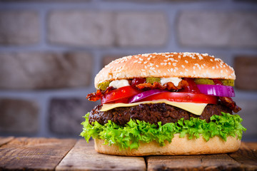 Delicious fresh hamburger on wooden table. Big burger in classic american style with hot grilled patty with melted cheese on top, tomato, onion and sauces.