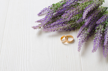 Wedding rings near bouquet of artificial purple lavender flowers on the wooden floor