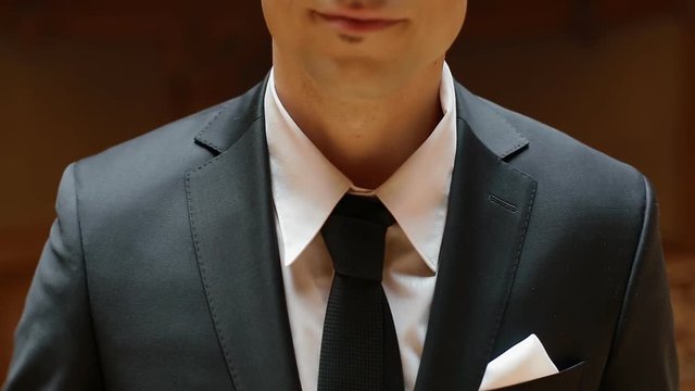 Portrait of young caucasian man in black suit indoor. Model corrects the tie.