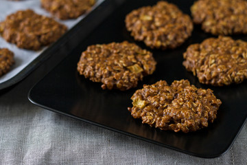 Homemade golden oatmeal cookies with apple and nuts on a black plate.