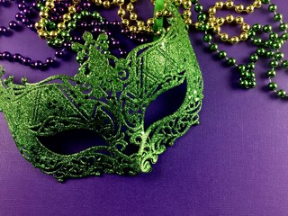 green mardi gras mask with beads on a purple surface