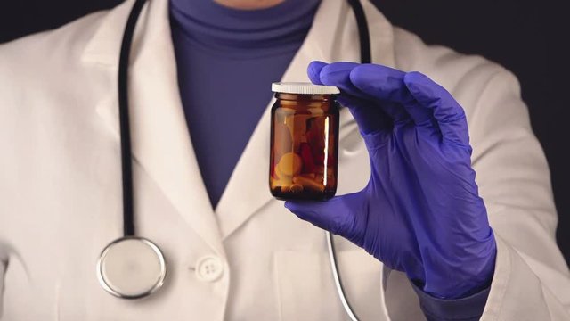 Female doctor unlabeled bottle of various pills and medications, close up of medical professional in white coat and protective gloves holding jar with tablets and painkillers