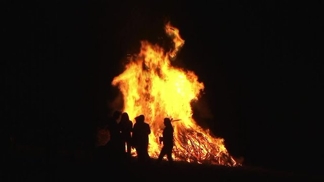 Silhouettenhaft sieht man Leute rund ums n&auml;chtliche Osterfeuer stehen