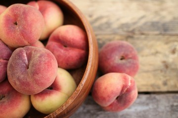 flat peaches in a wooden bowl on old wooden planks
