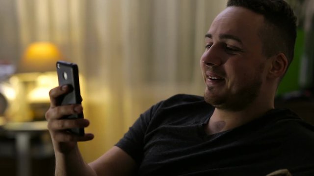 Young, happy man chatting on smartphone at home by night