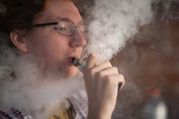Young man smoking electronic cigarette near window.