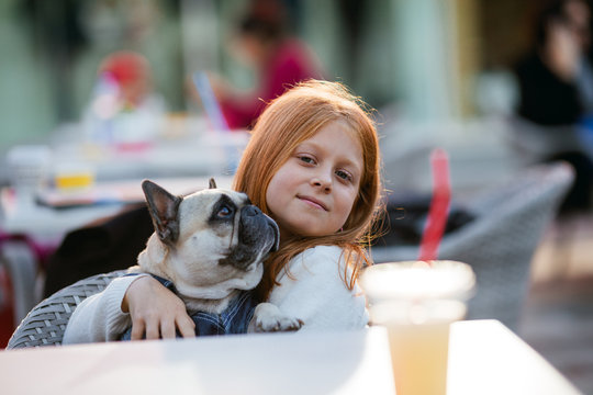 Beautiful young redhead girl holding adorable fawn french bulldog. 