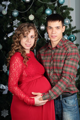 Young beautiful couple expecting baby together with Christmas tr