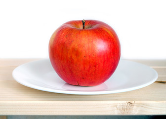 Big ripe apples on white plate in wooden shelf on white background front view closeup